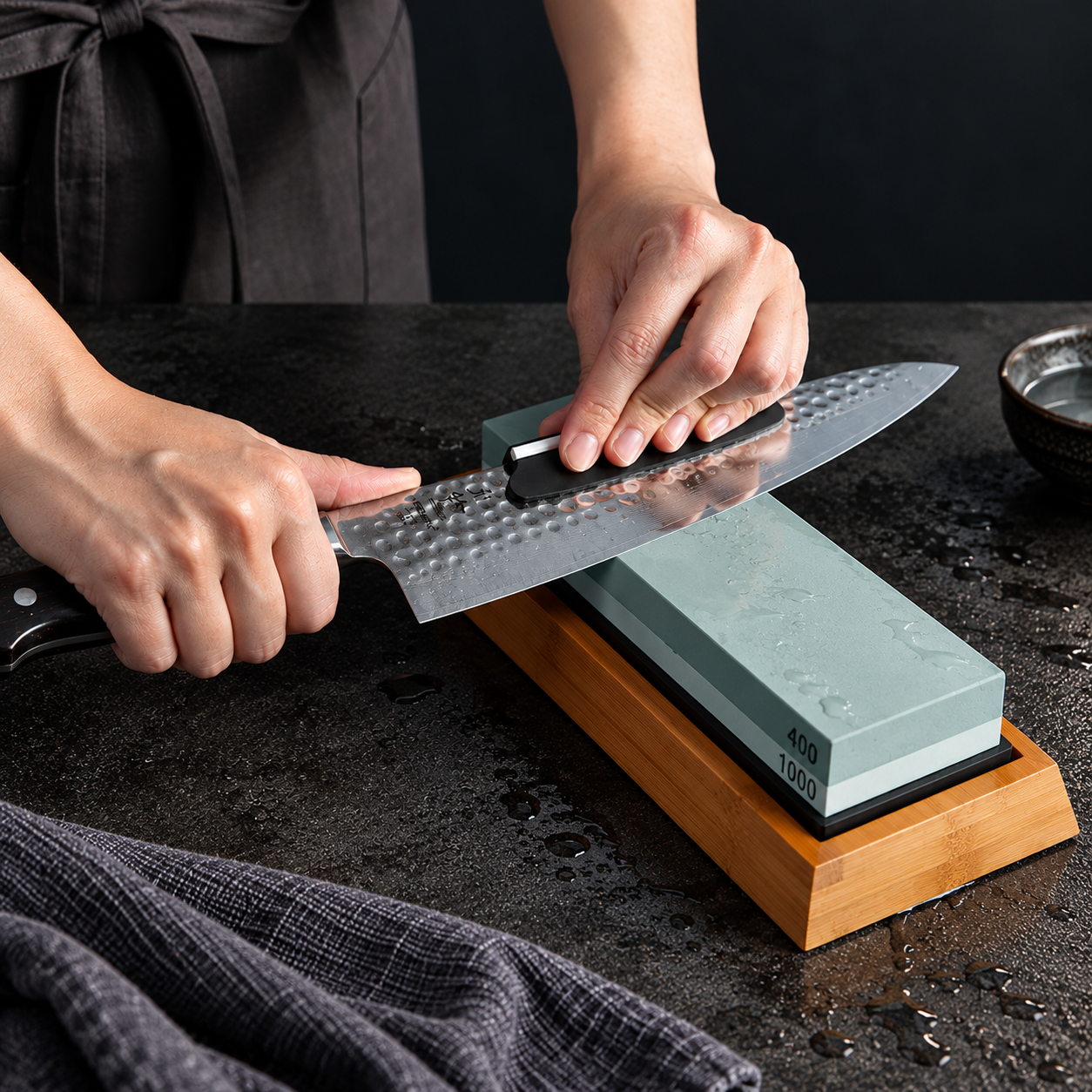Hands drawing a chef's knife across a wet Zoar whetstone in a bamboo base